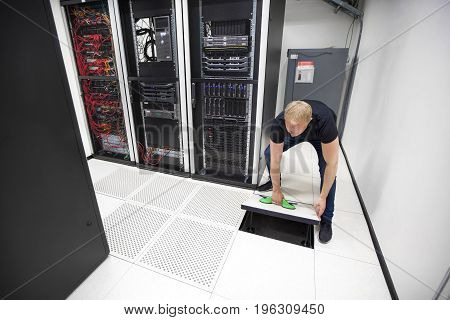 Full length of male IT engineer lifting floor tile using vacuum suction cups in datacenter