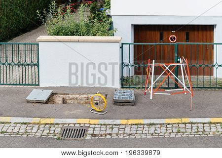 View from above of open sewage manhole hole with cable on coil spool - telecommunication internet provider company working on implementation of fiber optic cables in sewage system using fiber optic welding machine