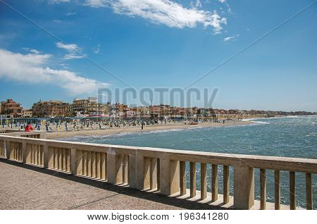 Ostia, Italy - May 18, 2013. View of marble pier, with the beach and the city of Ostia in the background, on a sunny day. The town is a seaside resort and ancient port of Rome. Lazio region