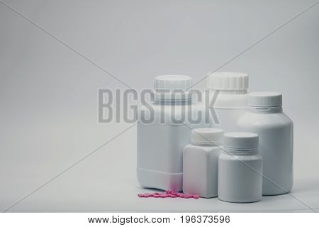 Pink tablet pills with closed bottle on white background
