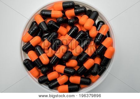 Top view of orange black capsule pills in plastic container on white background