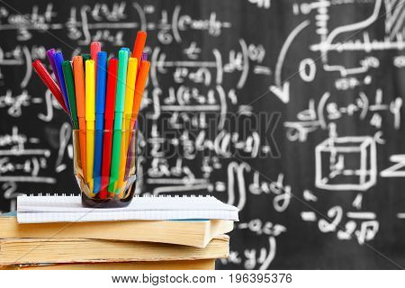 Back to school background with colorful pencils on the books and notebook and the title "Back to school" written by white chalk on the black school chalkboard