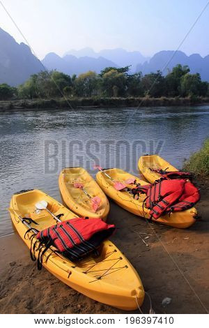Four yellow canoes with red life vest at riverside beach.