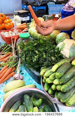 Fresh vegetables and herbs on the counter in the market. And a human hand with a carrot. Close-up.