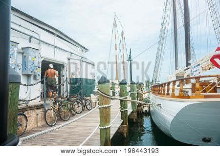 Key West , Florida, USA - June 26, 2012; Man standing bare backed in doorway of wharf shed with walkway and large sailing vessel moored alongside.