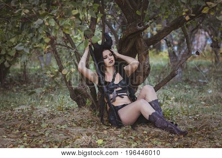 Pretty girl shaman with horns sits under a tree