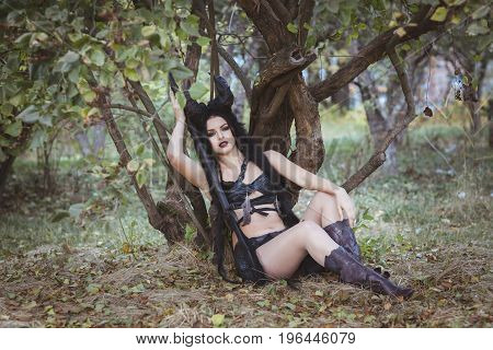 Beautiful girl shaman with horns sits under a tree