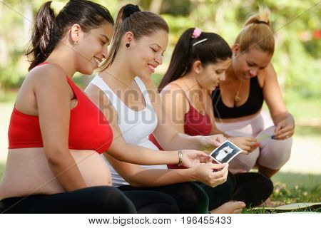 Pregnant women group of mothers during pregnancy. Lesson in city park with happy female friends smiling and looking at ecography scans.