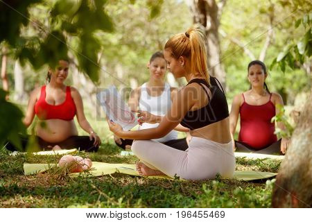 Pregnant women taking prenatal lesson in park. Teacher explaining baby growth inside belly with pictures and drawings.