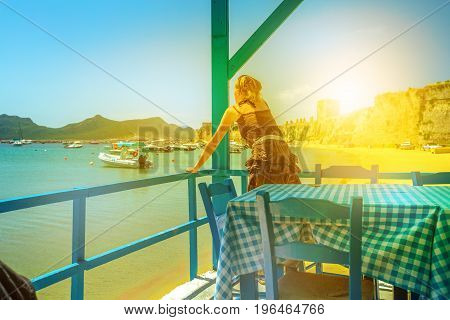Woman watching Methoni Castle at sunset from a porch on the Methoni beach. Peloponnese, Greece. Europe summer vacation.