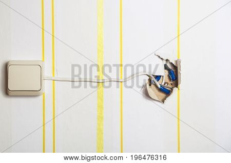 White light switch with a protruding wire on a white wall in yellow stripes