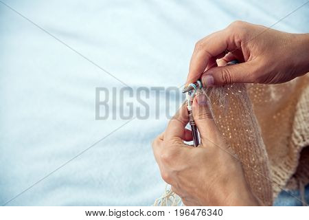 Close-up Young woman knits with knitting needles from pink woolen thread warm winter scarf on blue background