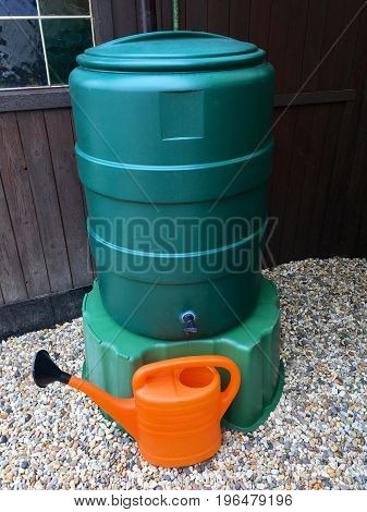 Big green water butt for rainwater with watering can in the garden