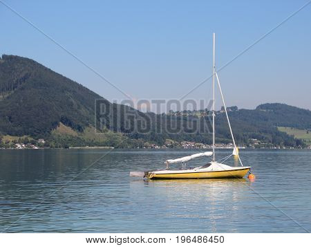 Yellow Sailboat on Blue Lake with Large Mountain Background in Summer
