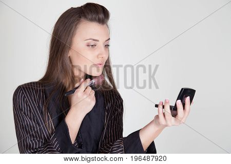 girl in coat makes brush makeup looks in the mirror 