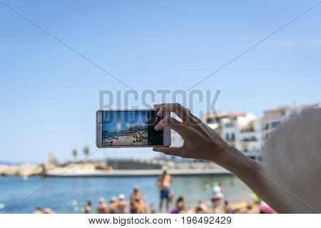 Hand held smartphone taking a picture in the urban beach of l'Escala. Costa Brava, Girona province, Spain.