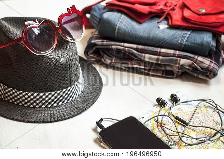 Travel accessories: hipster sneakers, denim shorts, plaid shirt, cowboy belt, hat, sungkasses, map and phone with headphones on wooden background. Selective focus. Traveling concept