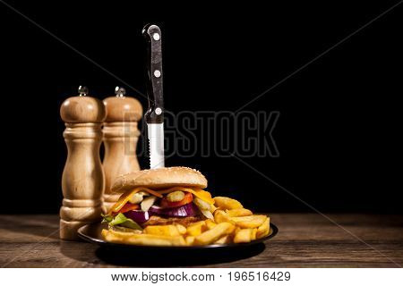 Classic home made cheesburgers on black plate and background next to fries. Fast food. Unhealthy snack