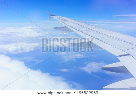 Looking thru airplane 's window seeing wing of airplane white clouds and blue sky