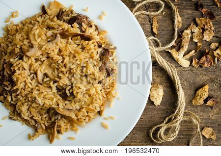 Homemade traditional Italian mushroom risotto on wooden table. Classic Risotto with mushrooms and vegetables served on a white plate. Wild mushrooms risotto. Top view.