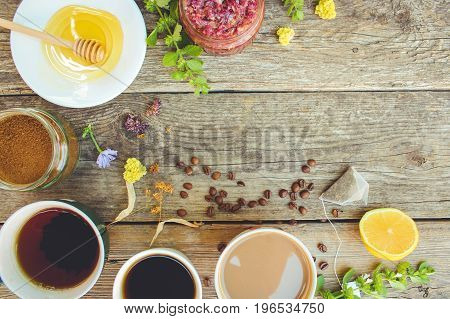 Tea, coffee, cocoa in cups, chicory, lemon, mint, jam made of rose petals, dried lime, honey on the old wooden background. Toned image. Top view.