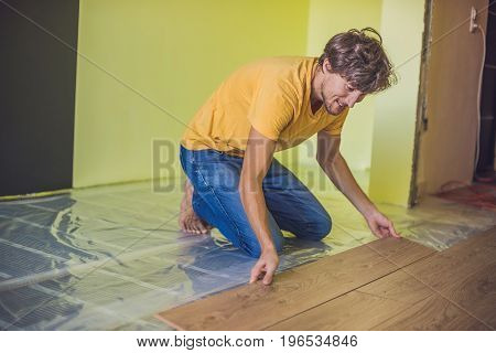 Man Installing New Wooden Laminate Flooring. Infrared Floor Heating System Under Laminate Floor