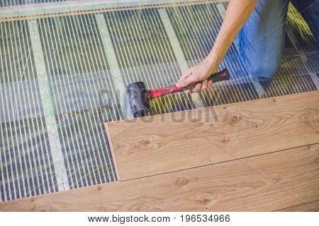 Man Installing New Wooden Laminate Flooring. Infrared Floor Heating System Under Laminate Floor