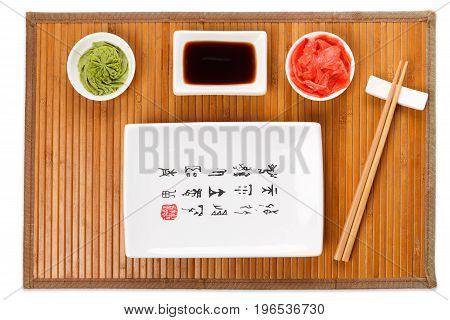 Set of sushi tablewear. Top view on empty rectangular sushi plate with hieroglyphs, saucer, ginger, wasabi and chopsticks on bamboo mat. Flat lay, copy space, background