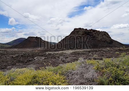 Two spatter cones and one cinder cone rising above a landscape of black volcanic basalt rock from eruptions along the Great Volcanic Rift Zone, a line of cones and lava vents. Craters of the Moon, USA