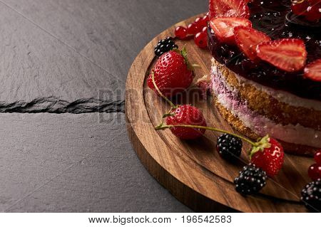 Fresh creamy patisserie cake with raspberries blackberries and strawberries on top. Dark stone background closeup.