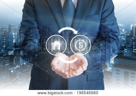 Business Man Holding Out Hands Under House And Money Exchanging Icons With Cityscape Background For