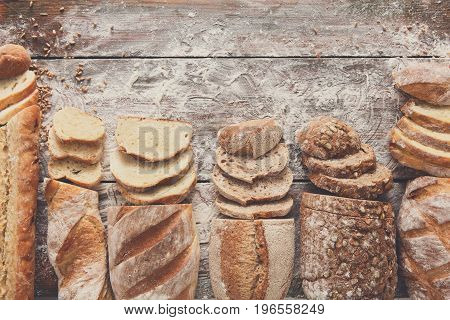 Sliced bread frame on rustic wood background, copy space. Brown and white loaves and flour top view composition with wheat flour sprinkled around.