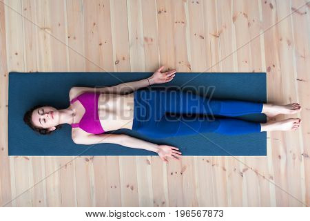 Top view of young woman lying in corpse or dead body pose relaxing after practicing yoga.