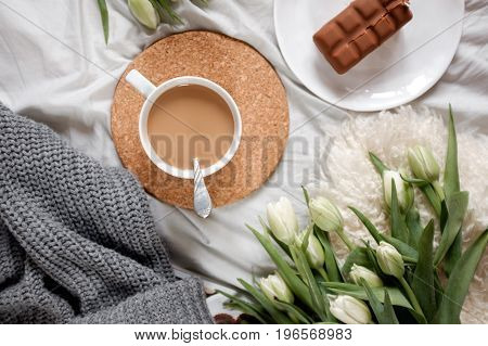 A cup of coffee next to a bouquet of tulips lies on a cozy tablecloth