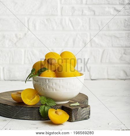 Yellow plums in a white ceramic bowl against a white kitchen brick wall. Selective focus