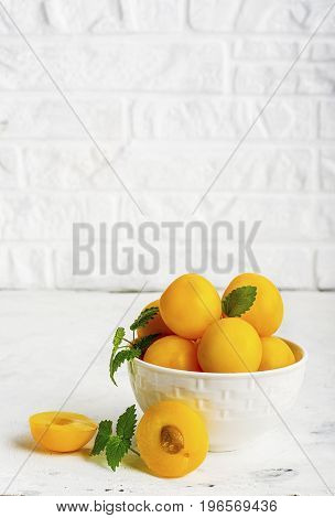 Yellow plums in a white ceramic bowl against a white kitchen brick wall. Selective focus