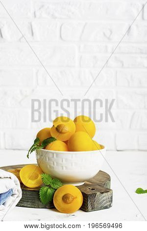 Yellow plums in a white ceramic bowl against a white kitchen brick wall. Selective focus
