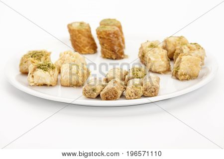 Crunchy Assabeh cashew baklava pieces arranged on a white plate. Dainty sweet dessert morsels made of flaky pastry as served in Middle Eastern cuisine. Closeup studio shot on bright table top.