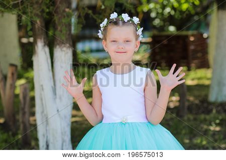Small cute girl in a blue and white dress raises his hands he said - hello child with a wreath of artificial flowers on her head