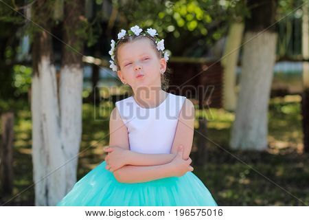 cute small girl flirting and embracing herselfchild with a wreath of artificial flowers on her head child in a festive dress on a nature background