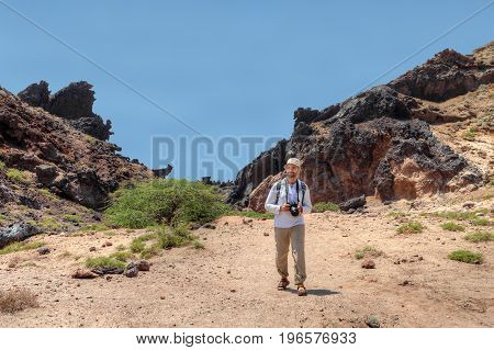 Iranian Island of Hormuz in Persian Gulf mature man tourist with a backpack and camera goes on mountain trail.