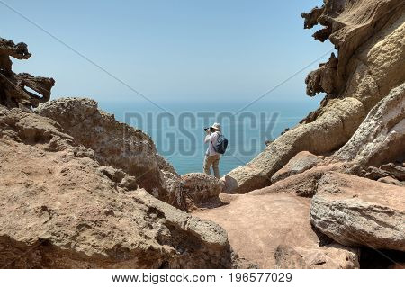 Tourist photographing nature standing on the edge of a cliff. Iranian Island of Hormuz in Persian Gulf Hormozgan Province southern Iran.