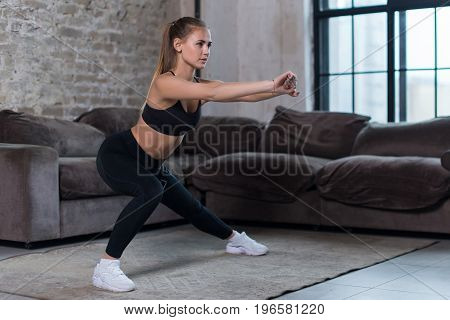 Beautiful fit girl doing home workout performing lateral lunges in a sitting room.