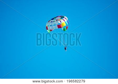 Parasailor on multi-colored parachute flying in blue clear sky sunny weather inspirational summer vacations freedom