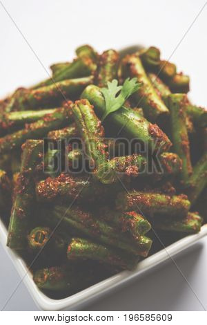 A Masala or fried vegetable dish consisting of green beans, onions, and curry spices, served in square bowl, selective focus