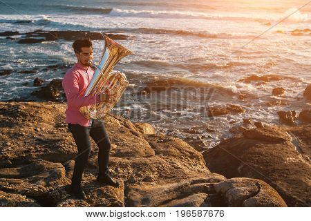 Tuba - instruments. Young man play the trumpet on rocky sea coast during surf.