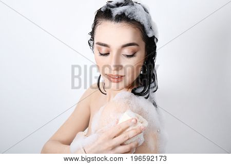 Young woman taking shower with bath puff on white background