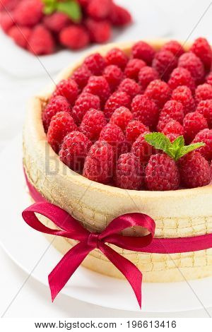 Birthday spongecake with raspberries decorated red ribbon and bow on a white background