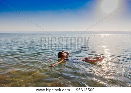 Girl floating on surface of Dead Sea Jordan enjoy her vacation during sunset time in summer. Concept for holiday travel lifestyle and wellness.