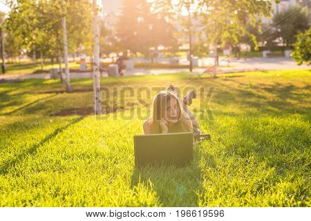 Young woman using laptop in the park lying on the green grass. Leisure time activity concept.